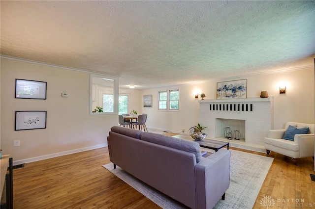 living area with a textured ceiling, wood finished floors, a fireplace, baseboards, and ornamental molding