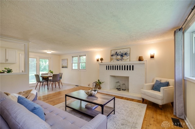living room featuring a textured ceiling, light wood finished floors, a fireplace, ornamental molding, and baseboards
