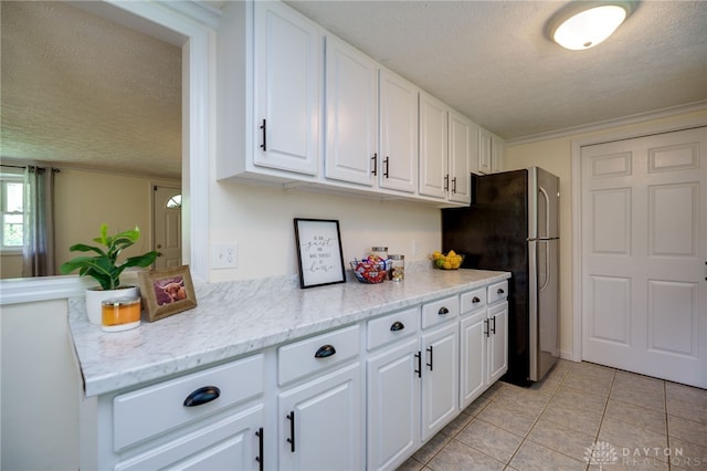 kitchen featuring a textured ceiling, freestanding refrigerator, white cabinetry, light tile patterned floors, and light stone countertops