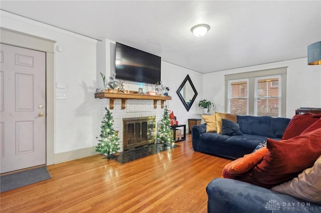 living room with hardwood / wood-style flooring, a brick fireplace, and crown molding