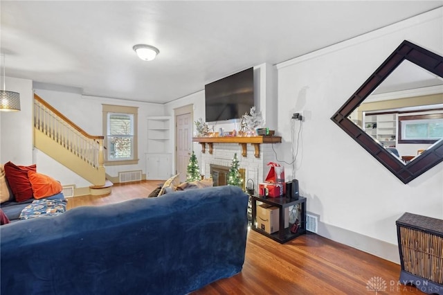 living room with a brick fireplace, hardwood / wood-style flooring, and built in features