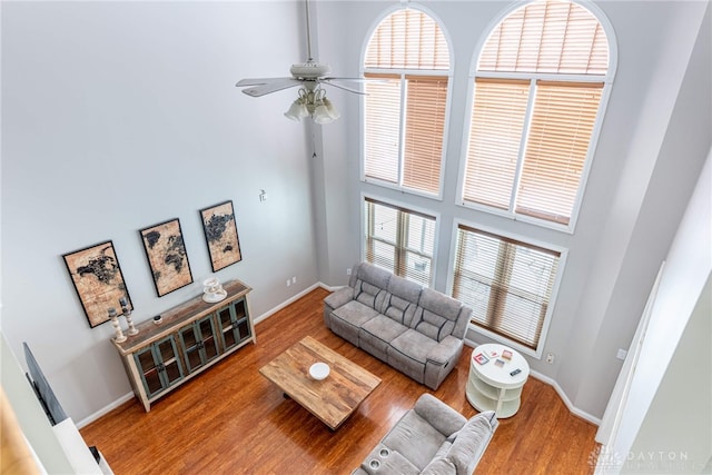 living room featuring wood-type flooring, a towering ceiling, and ceiling fan