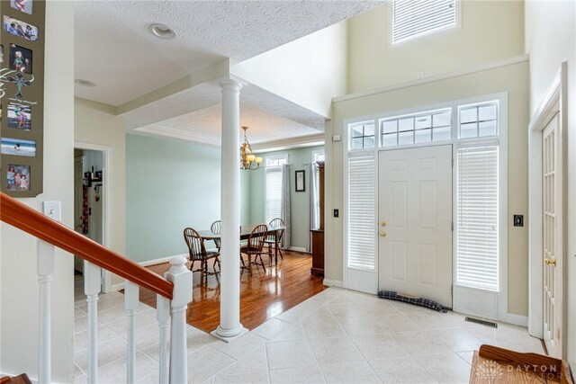 entryway featuring ornate columns, light tile patterned floors, a textured ceiling, and a chandelier