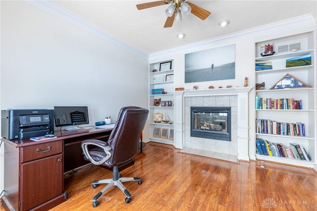 home office featuring a tile fireplace, built in shelves, crown molding, wood-type flooring, and a textured ceiling