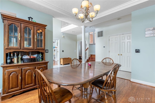 dining room featuring an inviting chandelier, light hardwood / wood-style flooring, decorative columns, a textured ceiling, and ornamental molding