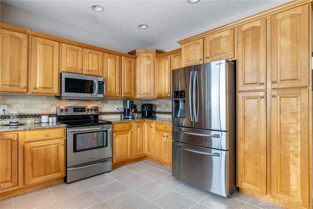 kitchen with decorative backsplash, light stone countertops, stainless steel appliances, and light tile patterned floors