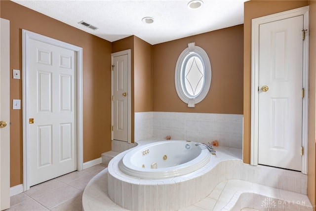 bathroom with a textured ceiling, tiled bath, and tile patterned floors