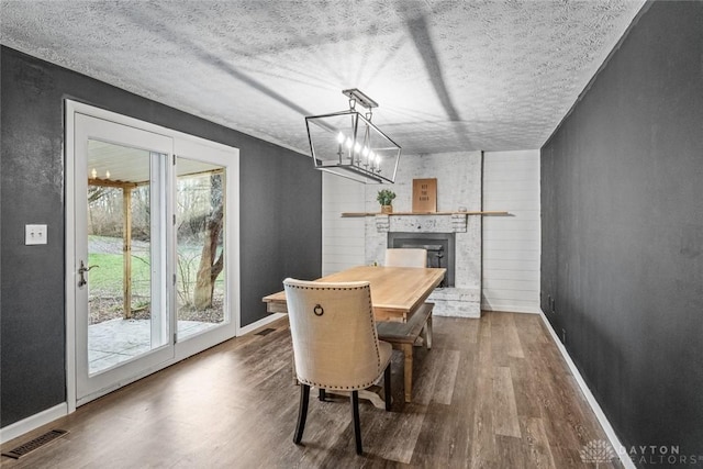 dining space featuring a large fireplace, dark hardwood / wood-style flooring, a notable chandelier, wood walls, and a textured ceiling