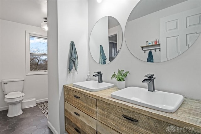 full bath with double vanity, baseboards, toilet, and a sink