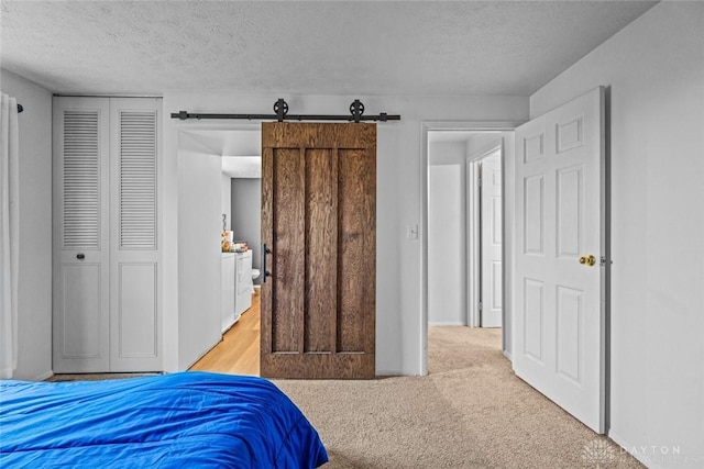 bedroom featuring a barn door, a textured ceiling, and light colored carpet