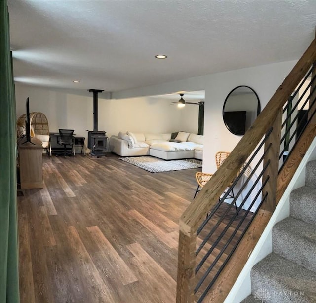 living room featuring a ceiling fan, wood finished floors, a wood stove, stairs, and recessed lighting