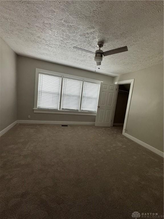 unfurnished room featuring ceiling fan, dark carpet, and a textured ceiling