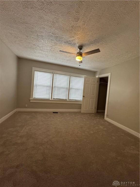 carpeted spare room featuring a wealth of natural light, ceiling fan, and a textured ceiling