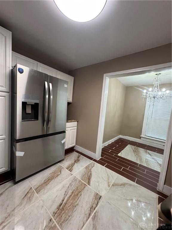 kitchen with stainless steel fridge, white cabinetry, and an inviting chandelier