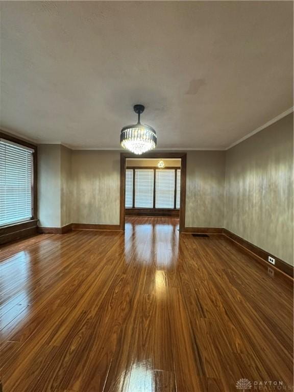 spare room featuring a chandelier, wood-type flooring, and crown molding