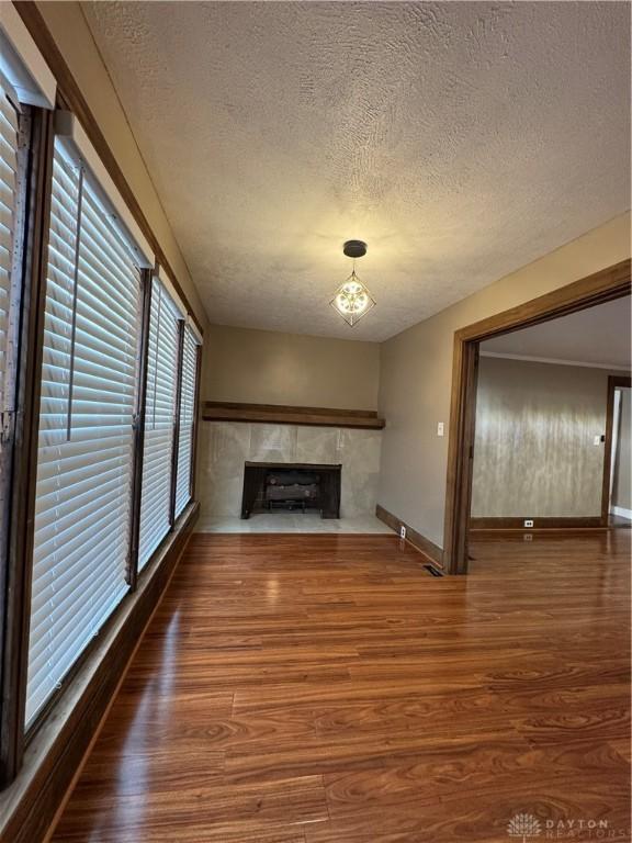 unfurnished living room with a tiled fireplace, a notable chandelier, a textured ceiling, and hardwood / wood-style flooring