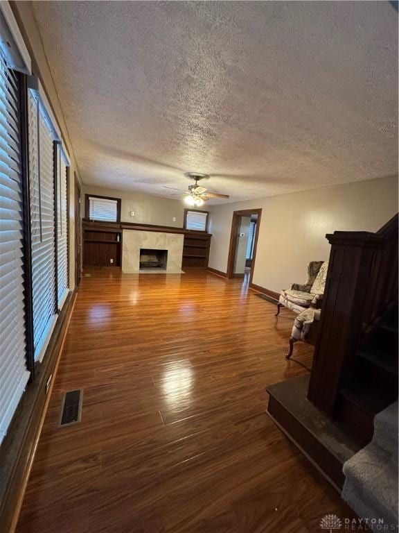 unfurnished living room with a healthy amount of sunlight, a tiled fireplace, ceiling fan, and wood-type flooring