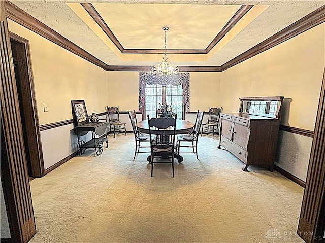 dining space with a tray ceiling, ornamental molding, light colored carpet, and a notable chandelier