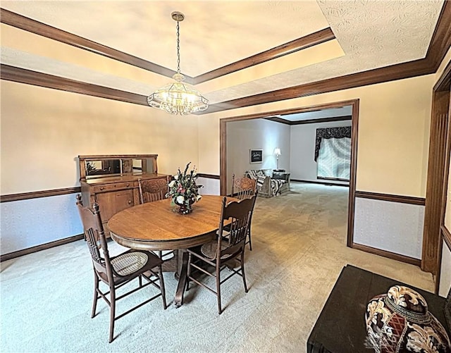 dining space featuring ornamental molding, light colored carpet, a tray ceiling, and a notable chandelier