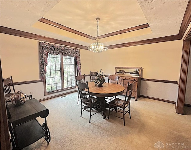 carpeted dining area featuring an inviting chandelier, ornamental molding, and a tray ceiling