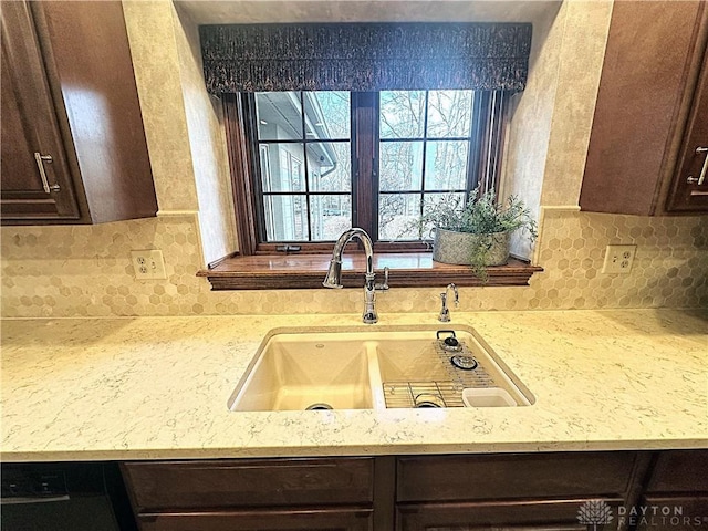 kitchen featuring dark brown cabinets, decorative backsplash, light stone countertops, and sink