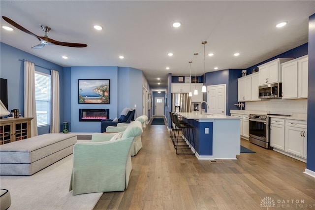 kitchen with white cabinets, appliances with stainless steel finishes, decorative light fixtures, and a kitchen island with sink