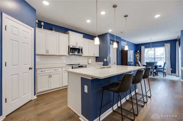 kitchen featuring white cabinets, a center island with sink, sink, tasteful backsplash, and decorative light fixtures