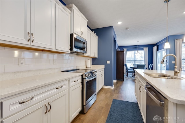 kitchen featuring sink, backsplash, light hardwood / wood-style floors, decorative light fixtures, and appliances with stainless steel finishes