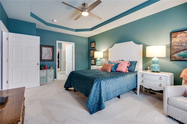 carpeted bedroom with ensuite bathroom, ceiling fan, and a tray ceiling