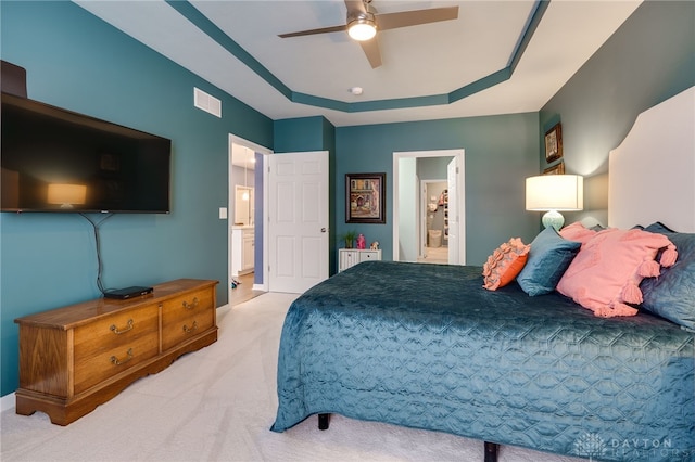 carpeted bedroom featuring ensuite bathroom, ceiling fan, and a tray ceiling