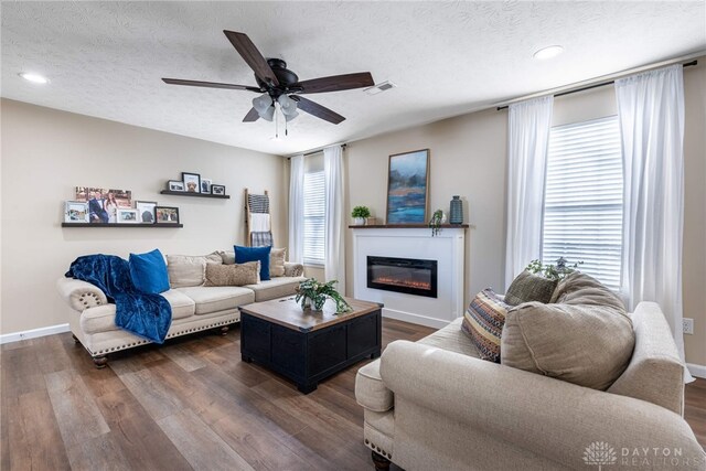 living room featuring a textured ceiling, a wealth of natural light, dark wood-type flooring, and ceiling fan