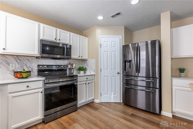 kitchen featuring tasteful backsplash, white cabinets, light hardwood / wood-style floors, and appliances with stainless steel finishes