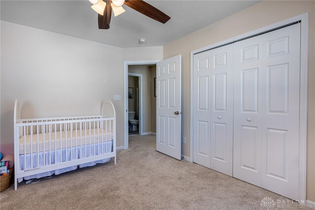 bedroom featuring ceiling fan, a closet, light carpet, and a crib