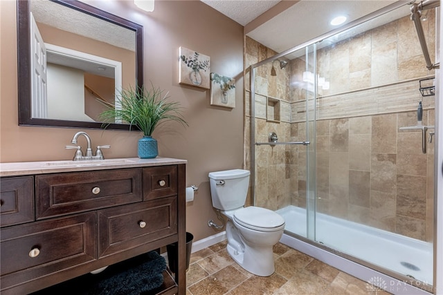 bathroom with vanity, toilet, a shower with shower door, and a textured ceiling