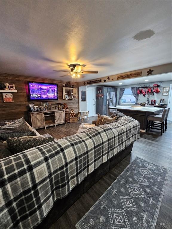 bedroom featuring stainless steel fridge with ice dispenser, wood walls, ceiling fan, and dark hardwood / wood-style floors