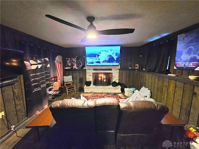 cinema with ceiling fan, wood walls, a stone fireplace, and a textured ceiling