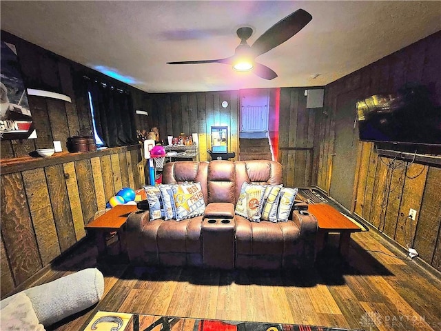 cinema room featuring ceiling fan, wood walls, and hardwood / wood-style flooring