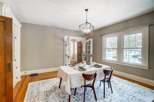 dining space with light wood-type flooring, a notable chandelier, and french doors