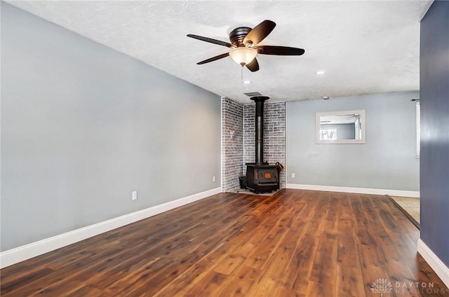 unfurnished living room featuring a wood stove, ceiling fan, dark wood-type flooring, and a textured ceiling