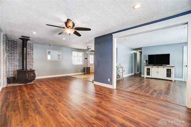 unfurnished living room featuring ceiling fan, wood-type flooring, a wood stove, and a textured ceiling