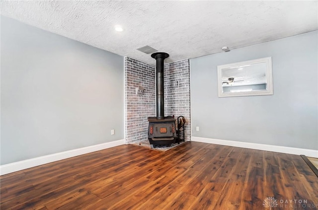 unfurnished living room featuring a wood stove, a textured ceiling, and hardwood / wood-style flooring