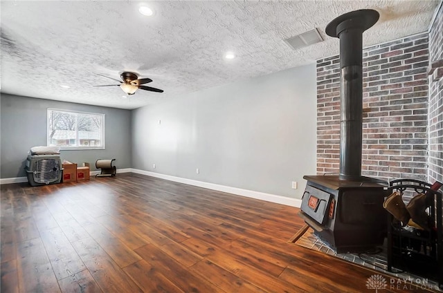 living room with a wood stove, ceiling fan, dark hardwood / wood-style floors, and a textured ceiling