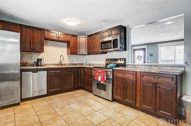 kitchen featuring light stone countertops, appliances with stainless steel finishes, a textured ceiling, sink, and light tile patterned flooring