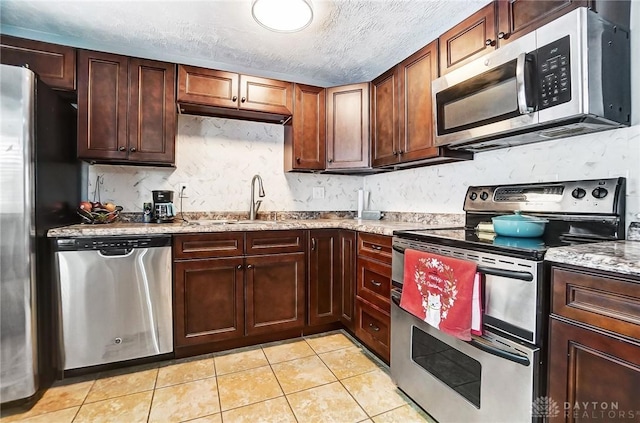 kitchen featuring light stone countertops, sink, stainless steel appliances, a textured ceiling, and light tile patterned floors