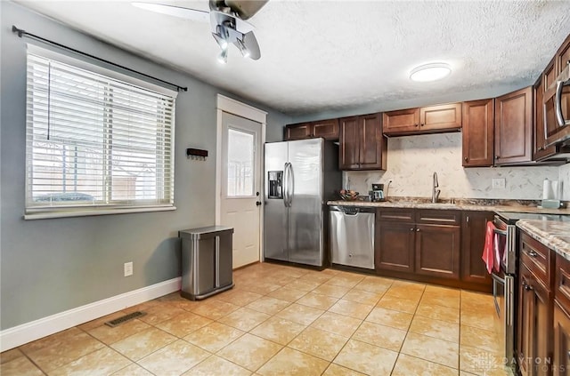 kitchen featuring sink, light tile patterned floors, a textured ceiling, light stone countertops, and appliances with stainless steel finishes