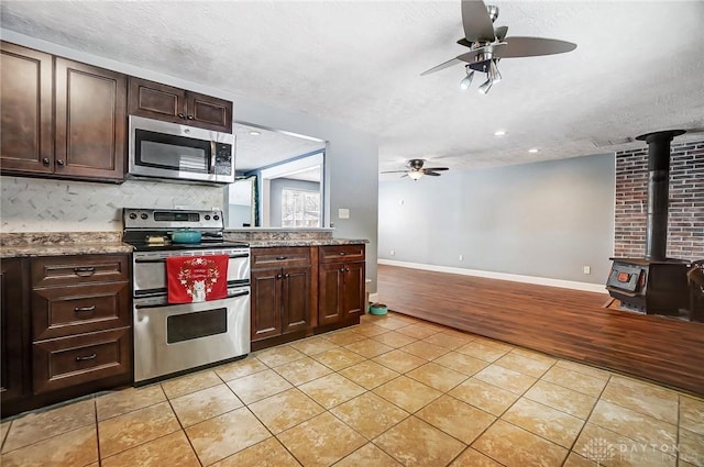 kitchen featuring a wood stove, dark brown cabinetry, stainless steel appliances, a textured ceiling, and light tile patterned flooring