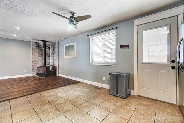 interior space featuring a wood stove, ceiling fan, light tile patterned floors, and a textured ceiling