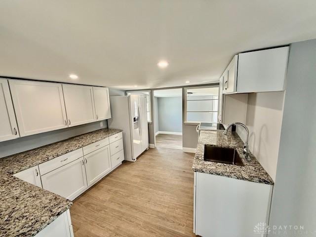 kitchen featuring sink, white cabinetry, white refrigerator with ice dispenser, light hardwood / wood-style floors, and dark stone counters