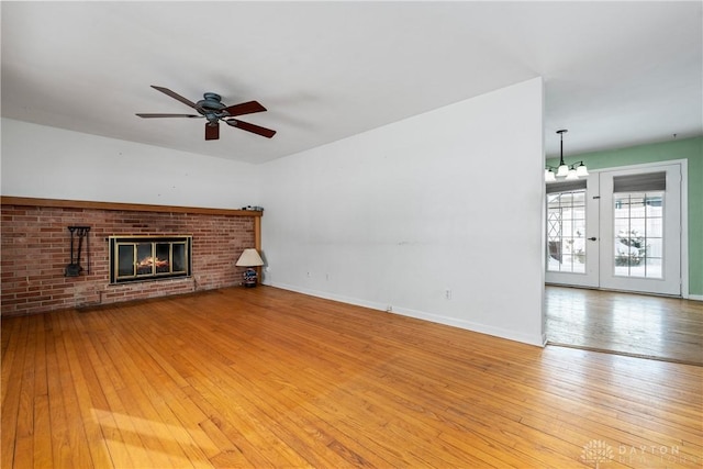 unfurnished living room with french doors, light hardwood / wood-style flooring, ceiling fan with notable chandelier, and a brick fireplace