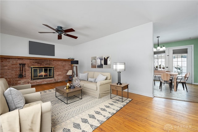 living room with ceiling fan with notable chandelier, light hardwood / wood-style floors, and a brick fireplace